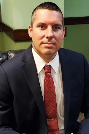 Headshot of Michael Krebs, a white male with black hair; he wears a dark blue suit jacket, a white button-up, and a red tie. 