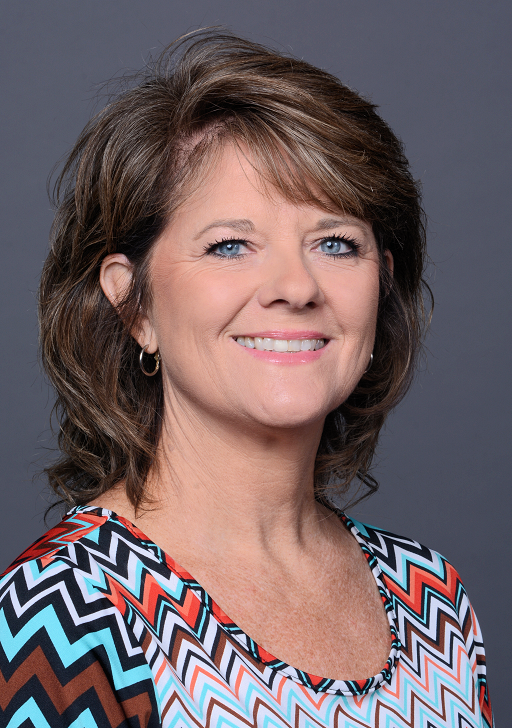 Headshot of Pam Harrison, a white female with brown hair; she wears a dark gray suit jacket and a white shirt. 