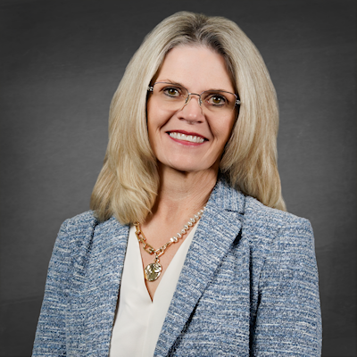 District Clerk Marci Gilbert, a Caucasian female with blonde hair and glasses, wearing a cream blouse, necklace, and blue and white business jacket.